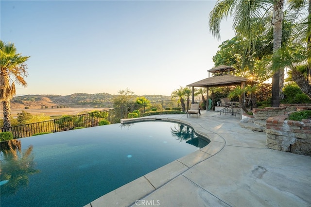 pool at dusk featuring a mountain view, a gazebo, and a patio