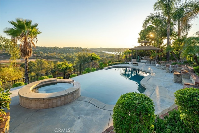 pool at dusk with a patio area and an in ground hot tub