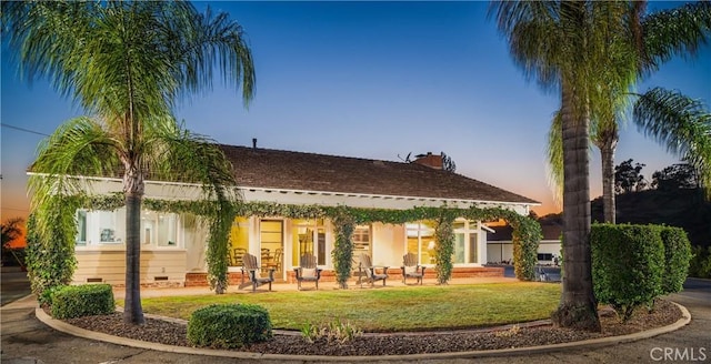 back house at dusk featuring a patio and a lawn