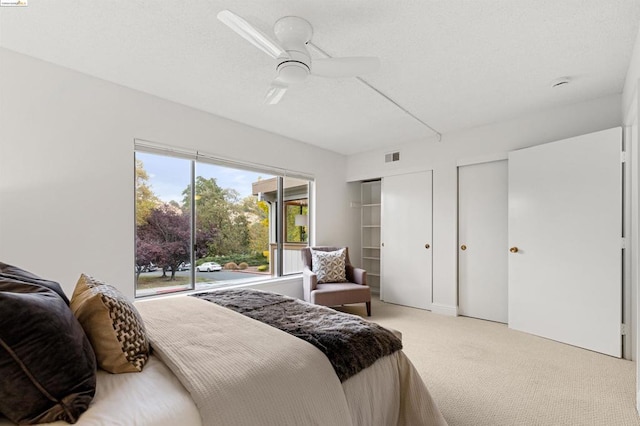 bedroom with multiple closets, ceiling fan, and light carpet