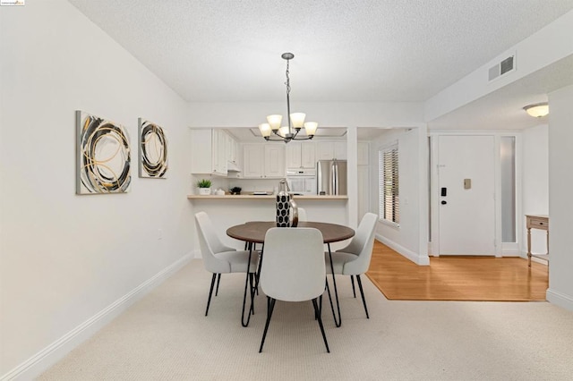 dining room with light hardwood / wood-style flooring, a textured ceiling, and an inviting chandelier