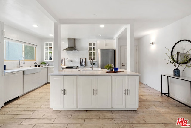 kitchen with stainless steel fridge, sink, wall chimney exhaust hood, and a kitchen island with sink