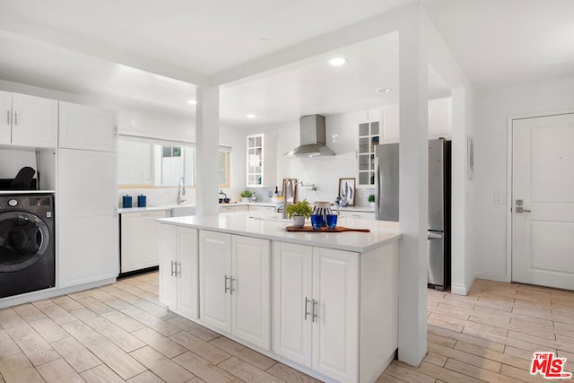 kitchen featuring washer / clothes dryer, white cabinets, wall chimney exhaust hood, and light wood-type flooring