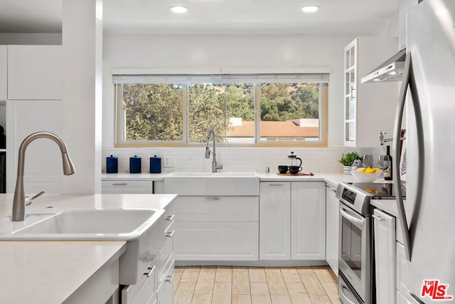 kitchen with white cabinets, ventilation hood, light hardwood / wood-style flooring, tasteful backsplash, and stainless steel appliances