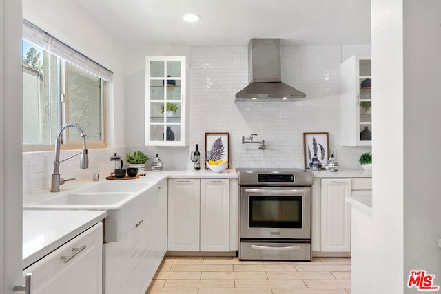 kitchen with wall chimney exhaust hood, white cabinetry, stainless steel electric range oven, and backsplash