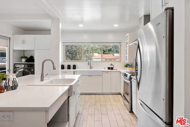 kitchen with appliances with stainless steel finishes, light wood-type flooring, tasteful backsplash, white cabinets, and washer / dryer