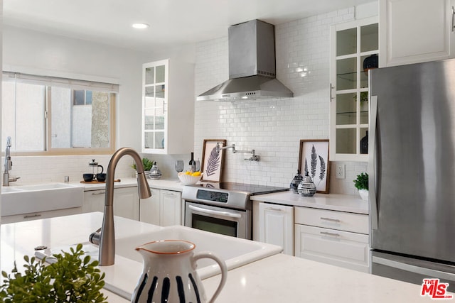 kitchen with decorative backsplash, stainless steel appliances, white cabinetry, and wall chimney range hood