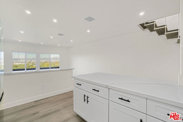 kitchen with light hardwood / wood-style floors, light stone counters, and white cabinetry