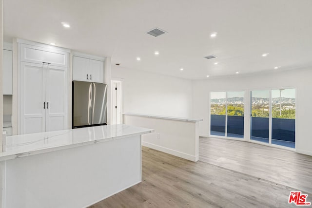 kitchen featuring stainless steel refrigerator, white cabinetry, a center island, light stone counters, and light hardwood / wood-style flooring