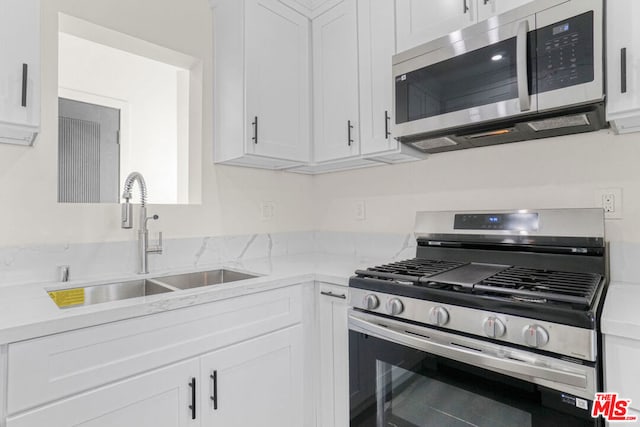 kitchen with white cabinets, appliances with stainless steel finishes, light stone counters, and sink