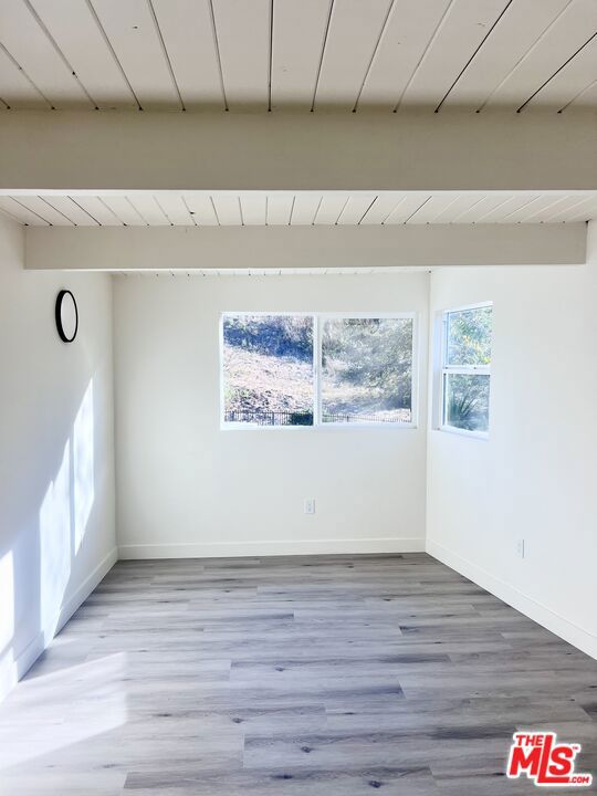 spare room featuring beam ceiling, light hardwood / wood-style flooring, and wood ceiling