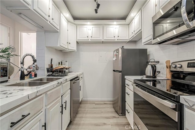 kitchen featuring light stone counters, stainless steel appliances, sink, light hardwood / wood-style flooring, and white cabinetry