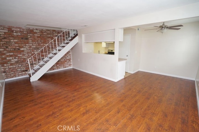 unfurnished living room with ceiling fan, dark wood-type flooring, and brick wall