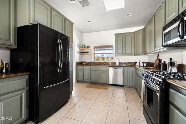 kitchen with light tile patterned floors, black appliances, sink, and green cabinetry