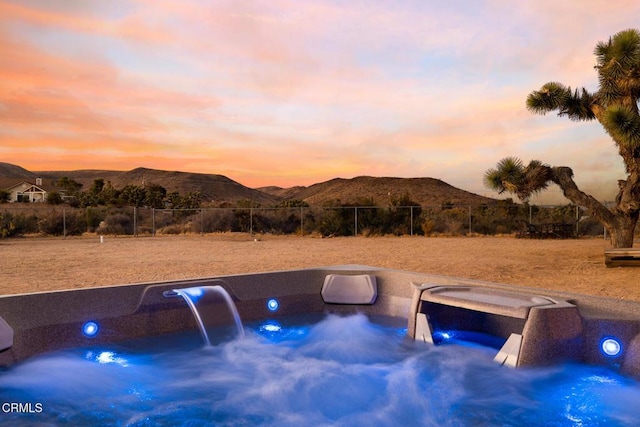 pool at dusk featuring an outdoor hot tub and a mountain view