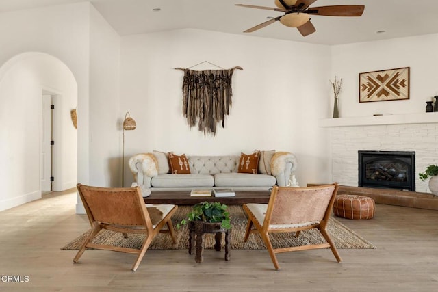 living room featuring a tiled fireplace, ceiling fan, and light hardwood / wood-style floors