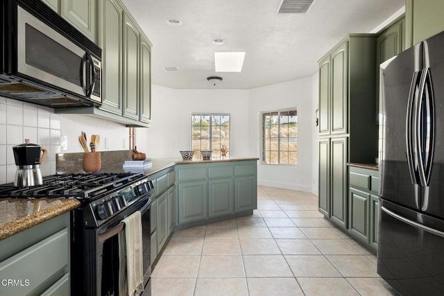 kitchen featuring green cabinets, appliances with stainless steel finishes, light tile patterned flooring, kitchen peninsula, and dark stone counters