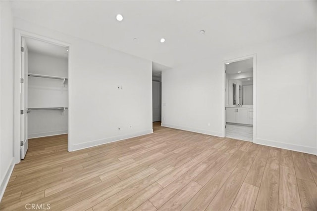 unfurnished bedroom featuring a walk in closet, ensuite bathroom, a closet, and light hardwood / wood-style floors