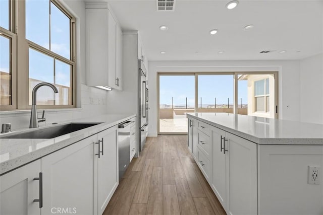 kitchen with white cabinets, a healthy amount of sunlight, light hardwood / wood-style floors, and sink