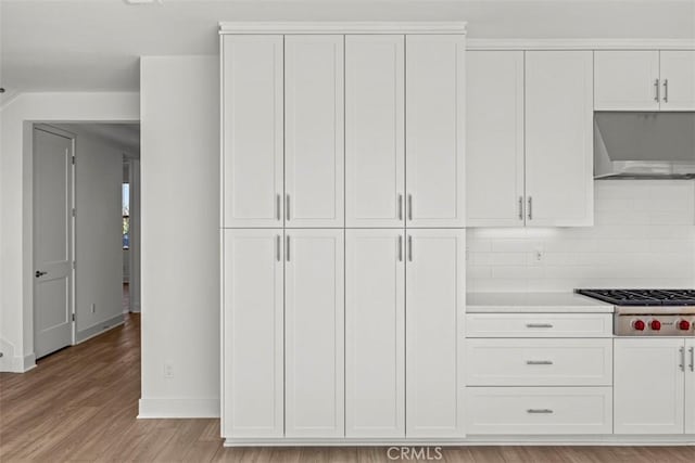 kitchen with white cabinetry, wall chimney exhaust hood, light hardwood / wood-style floors, stainless steel gas stovetop, and decorative backsplash