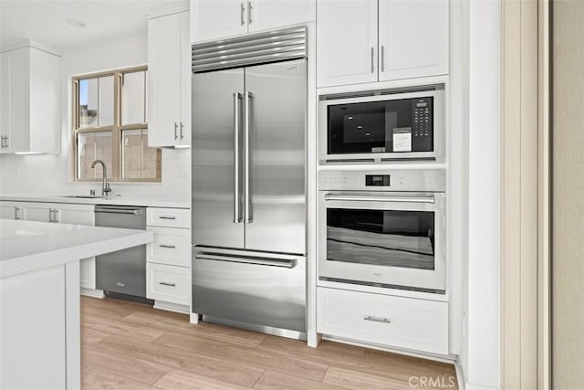 kitchen featuring built in appliances, white cabinets, and light wood-type flooring