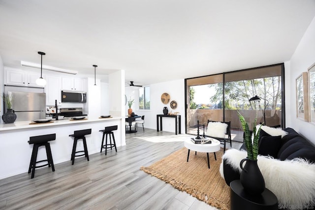 living room featuring ceiling fan, a wealth of natural light, light wood-type flooring, and a wall of windows