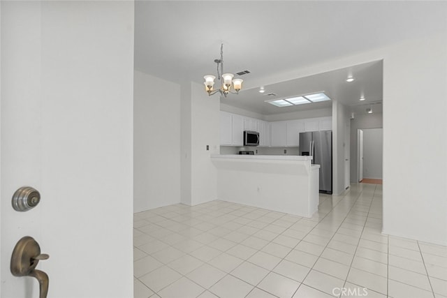 kitchen with kitchen peninsula, appliances with stainless steel finishes, light tile patterned floors, an inviting chandelier, and white cabinets