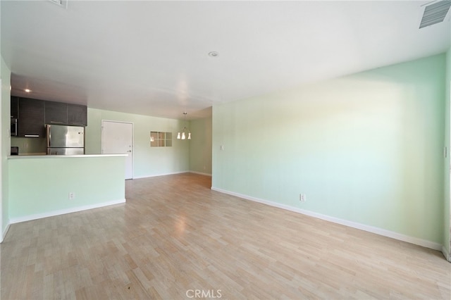 unfurnished living room featuring a chandelier and light wood-type flooring