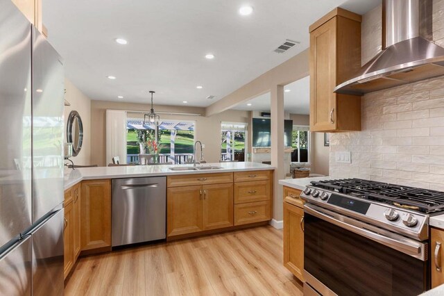 kitchen with sink, hanging light fixtures, wall chimney exhaust hood, stainless steel appliances, and light hardwood / wood-style flooring