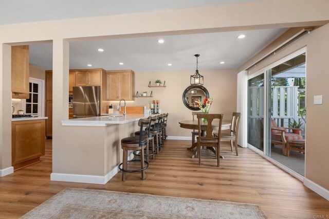 kitchen with sink, stainless steel fridge, light hardwood / wood-style floors, and kitchen peninsula