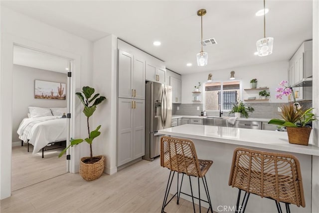 kitchen featuring kitchen peninsula, stainless steel appliances, tasteful backsplash, decorative light fixtures, and light wood-type flooring