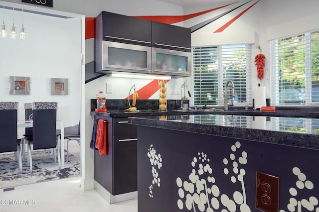 kitchen with decorative light fixtures, dark stone countertops, light tile patterned floors, and sink