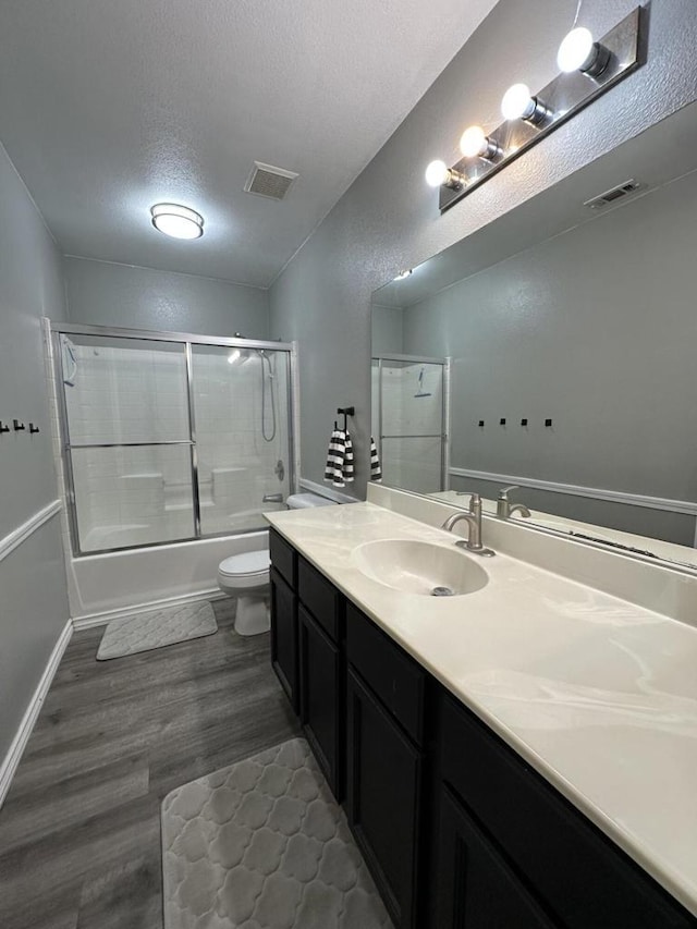 full bathroom with toilet, bath / shower combo with glass door, vanity, hardwood / wood-style floors, and a textured ceiling