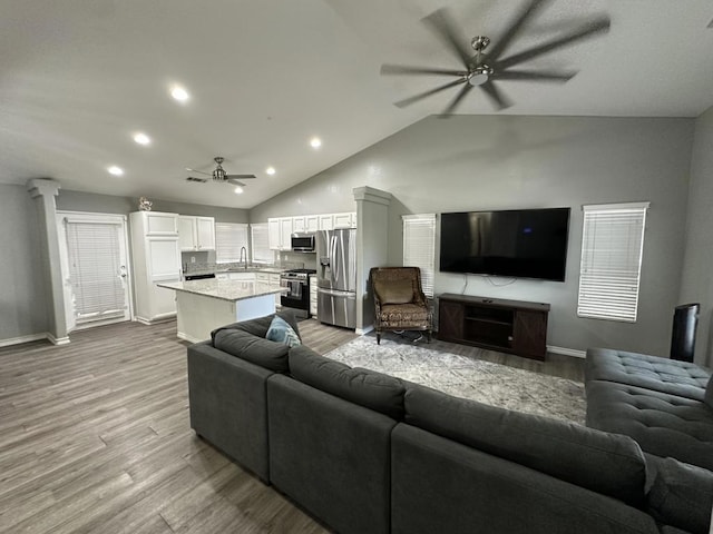 living room featuring light wood-type flooring, vaulted ceiling, sink, and ceiling fan