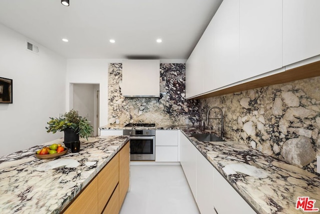 kitchen featuring light stone countertops, tasteful backsplash, stainless steel oven, sink, and white cabinetry