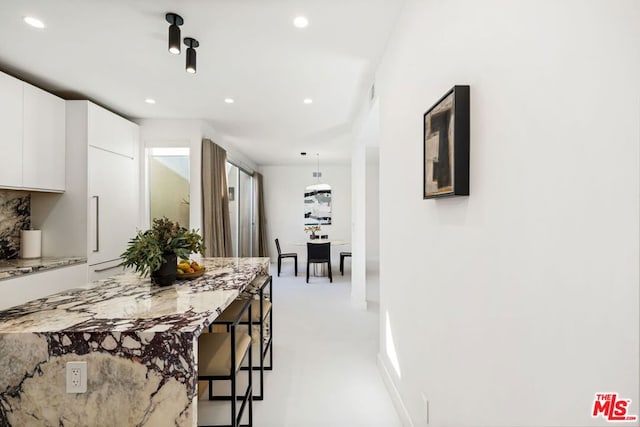 kitchen featuring decorative backsplash, light stone countertops, a breakfast bar, white cabinets, and hanging light fixtures