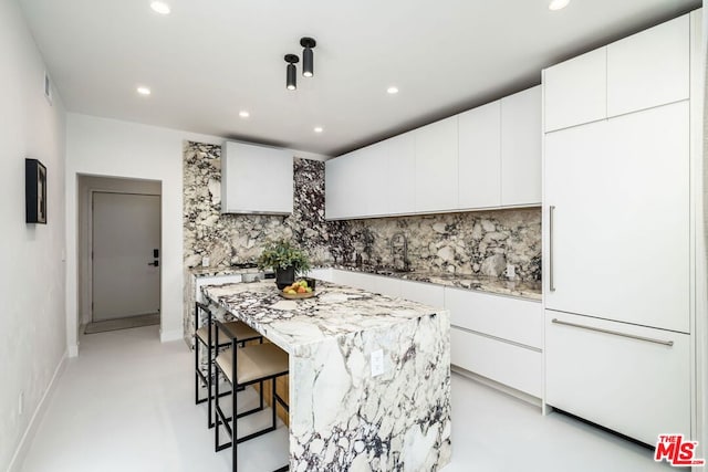 kitchen featuring white cabinetry, sink, tasteful backsplash, a breakfast bar, and a kitchen island