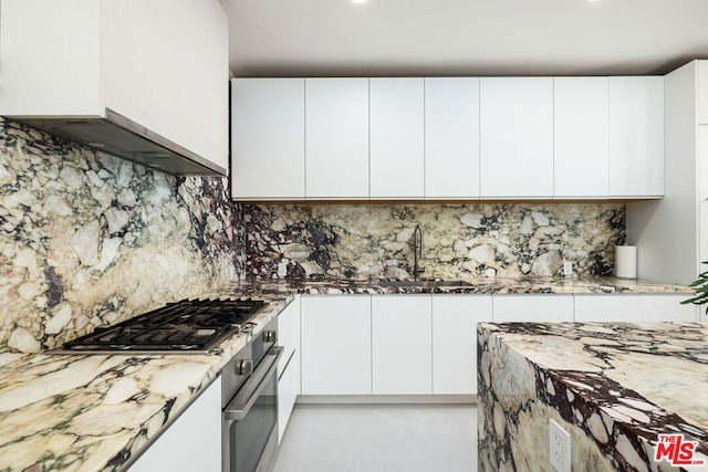 kitchen featuring white cabinets, light stone counters, and backsplash