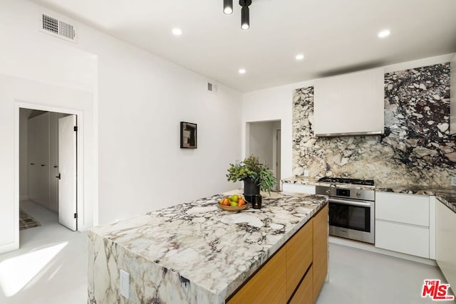 kitchen with light stone countertops, ventilation hood, stainless steel appliances, white cabinets, and a center island