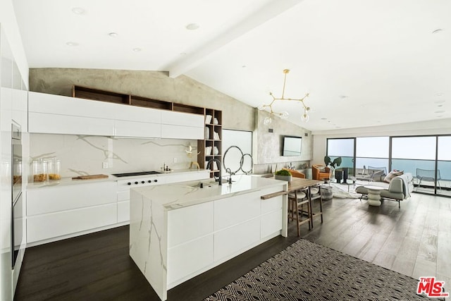 kitchen featuring dark hardwood / wood-style flooring, lofted ceiling with beams, white cabinetry, and a kitchen island with sink