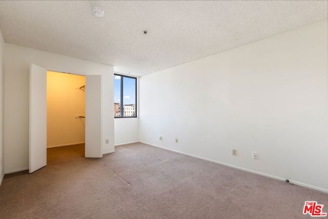 unfurnished bedroom featuring a walk in closet, a closet, carpet floors, and a textured ceiling