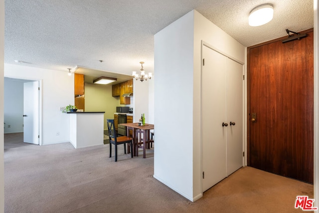 corridor featuring a textured ceiling, light colored carpet, and an inviting chandelier