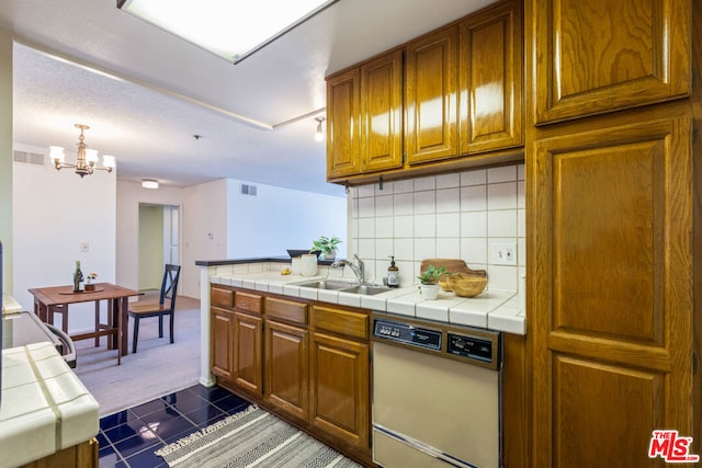 kitchen featuring dishwasher, backsplash, sink, tile counters, and a chandelier