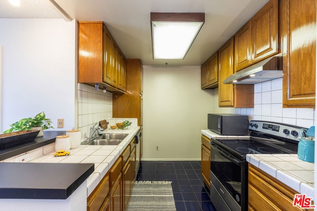 kitchen with sink, stainless steel appliances, dark tile patterned floors, tile countertops, and decorative backsplash