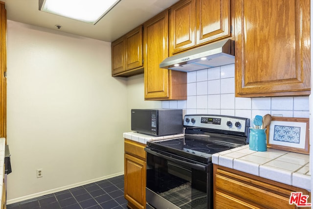 kitchen featuring dark tile patterned floors, tile countertops, stainless steel electric range oven, and tasteful backsplash