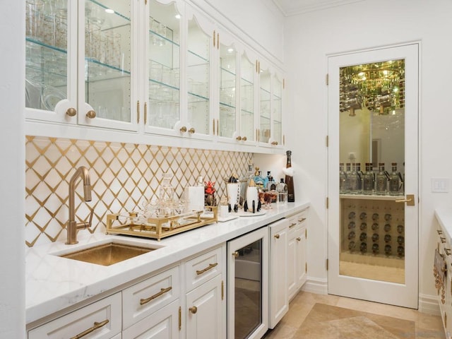 bar with white cabinetry, sink, light stone countertops, beverage cooler, and backsplash