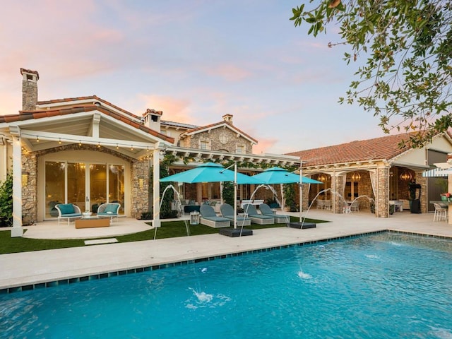 pool at dusk featuring pool water feature, an outdoor hangout area, and a patio area