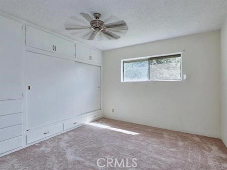 carpeted empty room featuring a textured ceiling and ceiling fan