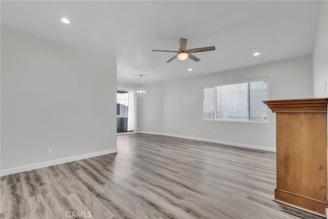 unfurnished living room with ceiling fan with notable chandelier, a healthy amount of sunlight, and light hardwood / wood-style flooring