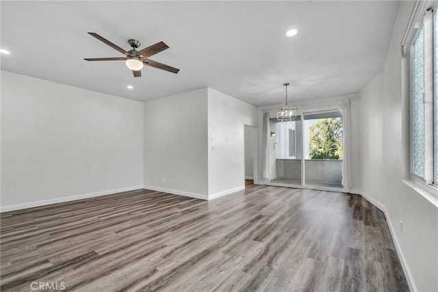 empty room featuring a wealth of natural light, wood-type flooring, and ceiling fan with notable chandelier